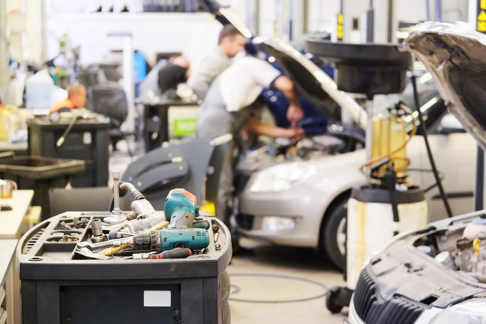 Atelier de réparation automobile avec mécaniciens en combinaison travaillant sur véhicules, capots ouverts