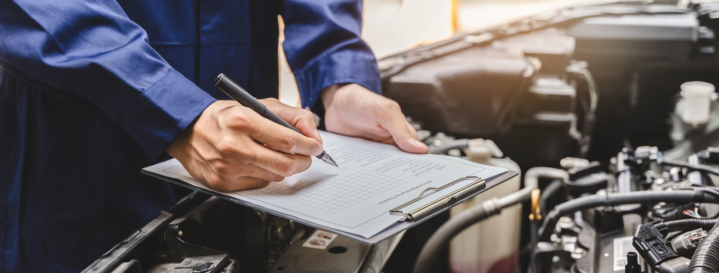 Mécanicien automobile en combinaison bleue effectuant la maintenance d'un moteur dans un garage professionnel
