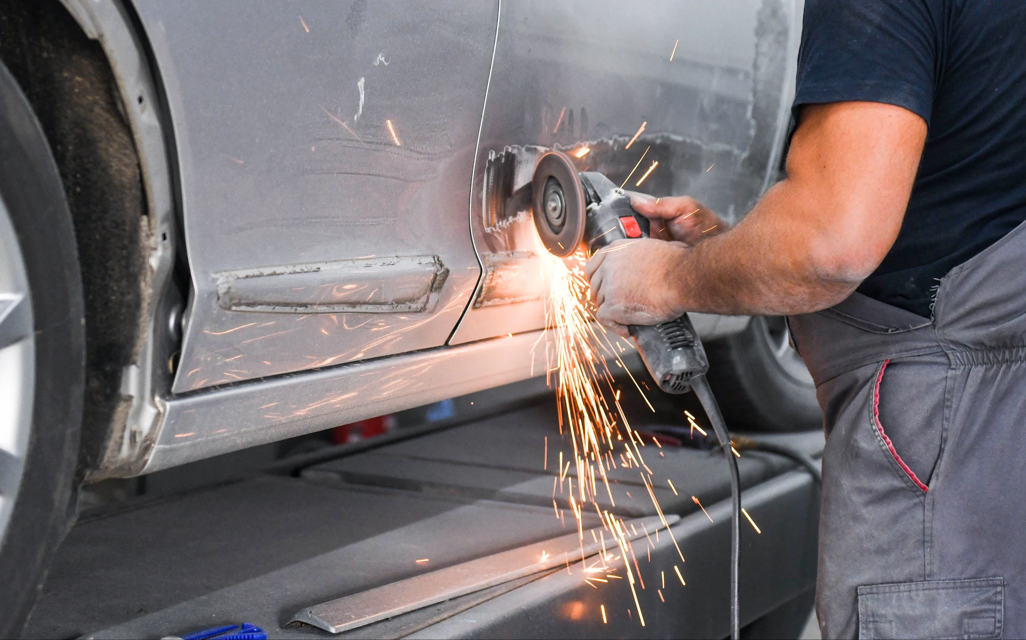 Atelier de carrosserie automobile, technicien utilisant une meuleuse d'angle sur carrosserie de véhicule blanc