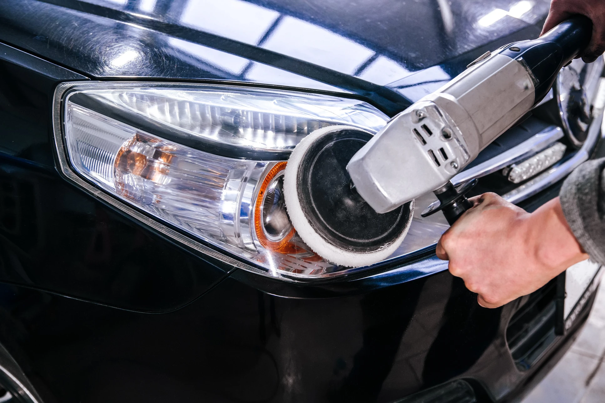 Atelier automobile, technicien utilisant une polisseuse orbitale sur carrosserie rouge d'un véhicule