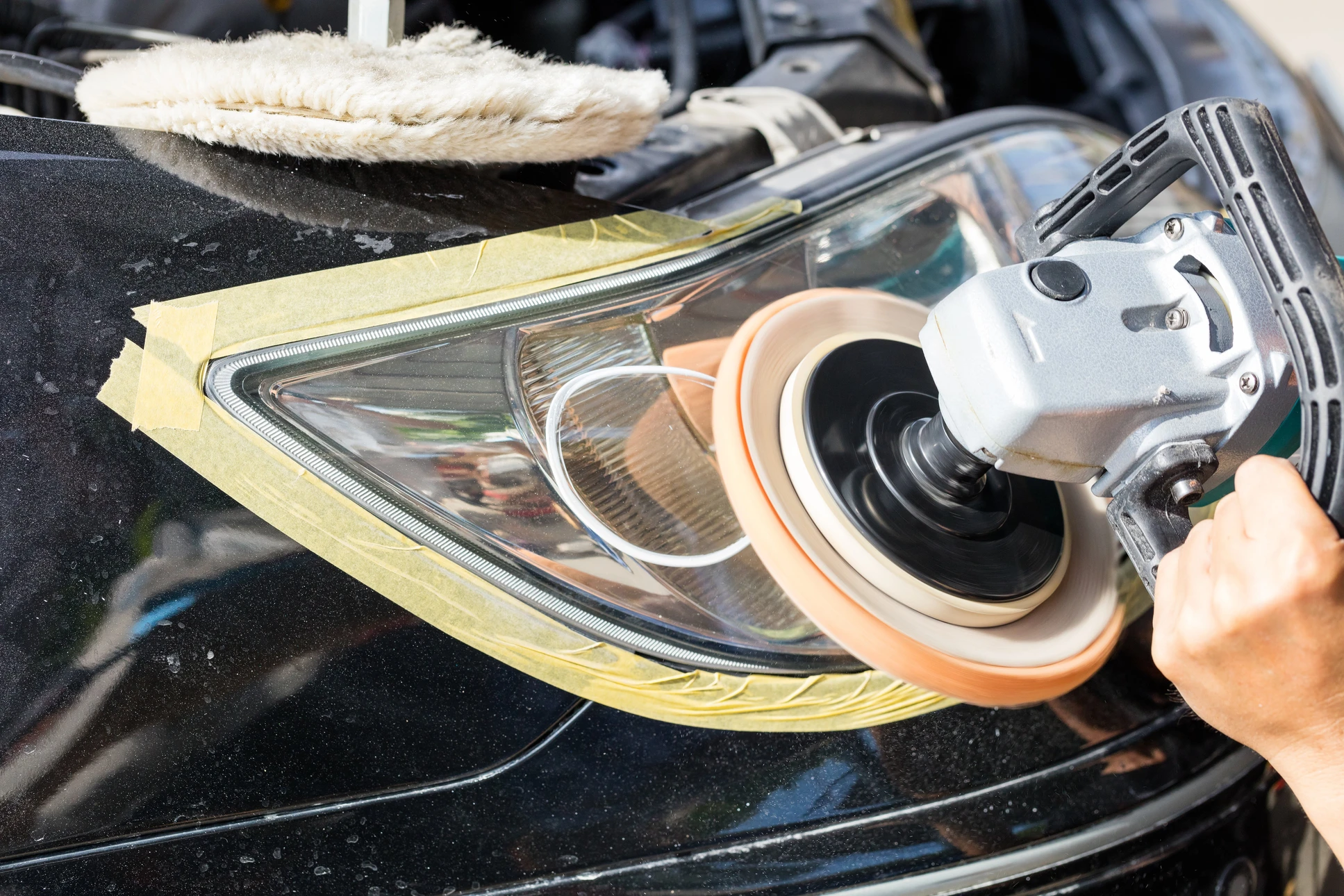 Professionnel en tenue de travail utilisant une polisseuse orbitale électrique sur la carrosserie d'un véhicule blanc dans un atelier automobile